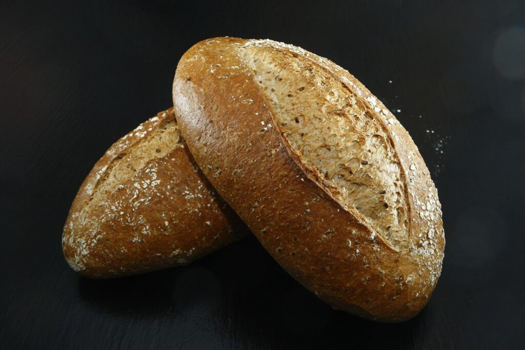 Two artisanal whole-grain bread loaves on a dark surface, perfect for healthy dining.